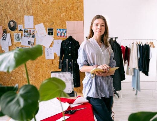 Fashion designer standing in a creative studio surrounded by clothing and sketches.
