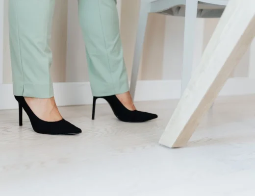 Close-up of elegant black high heels paired with mint green pants on a light wooden floor.