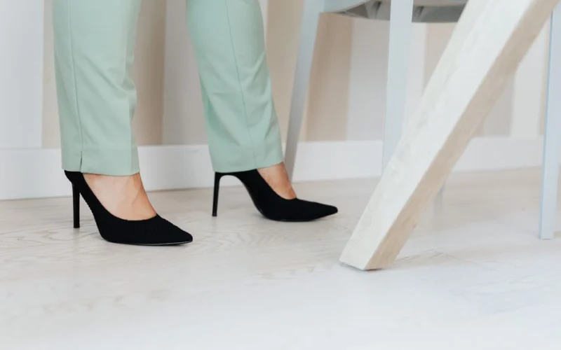 Close-up of elegant black high heels paired with mint green pants on a light wooden floor.