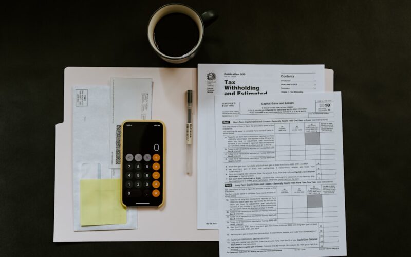 black Android smartphone near ballpoint pen, tax withholding certificate on top of white folder