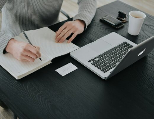 A person in a grey sweater writing in a notebook at a black desk