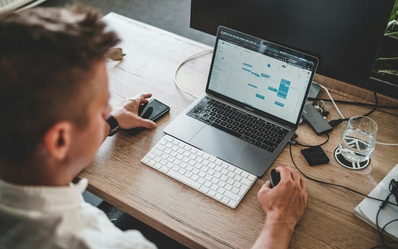 man holding mouse and iPhone while using Macbook Pro