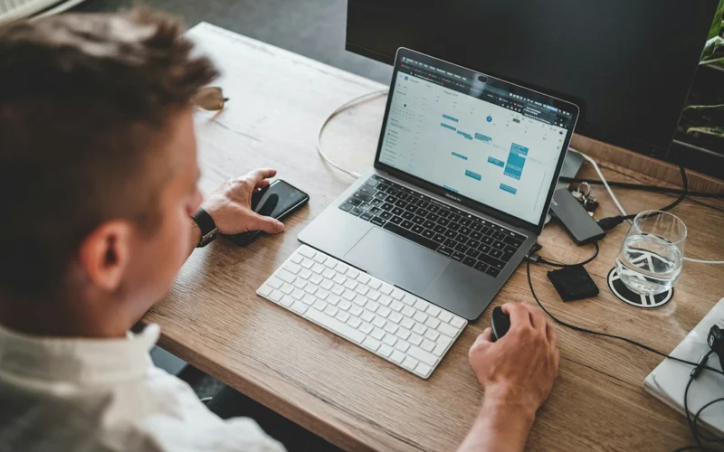 man holding mouse and iPhone while using Macbook Pro